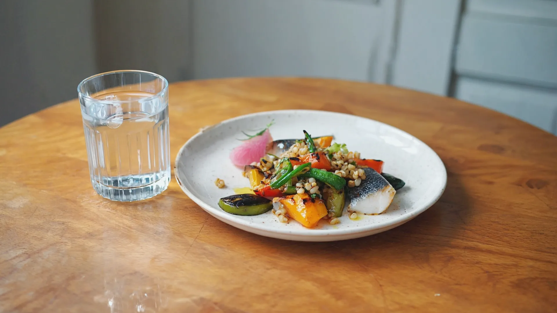 Orlistat is taken with main meals, alongside a lower-fat diet A glass of water beside a plate of grilled vegetables, grains and fish on a wooden table