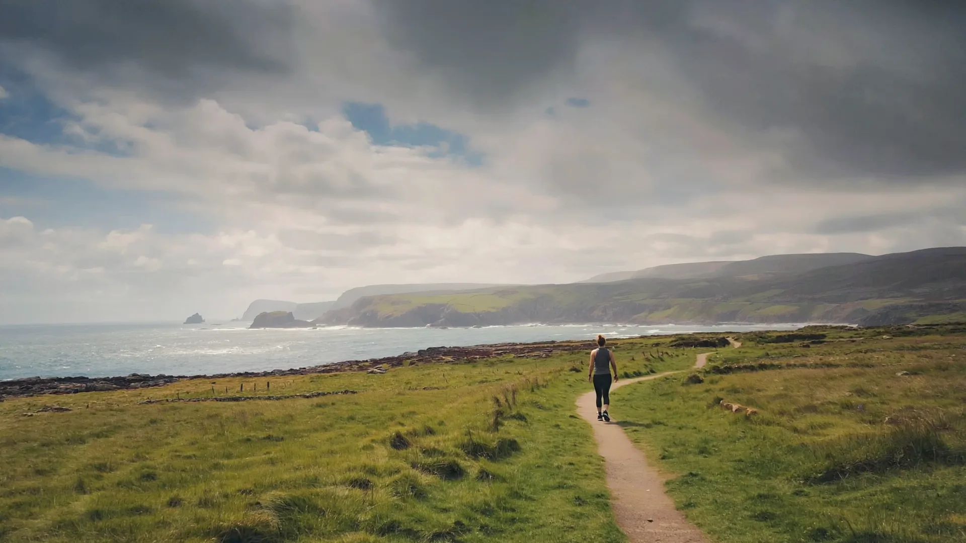 A person walking briskly along a green coastal path in Ireland on a bright day A person walking briskly along a green coastal path in Ireland on a bright day