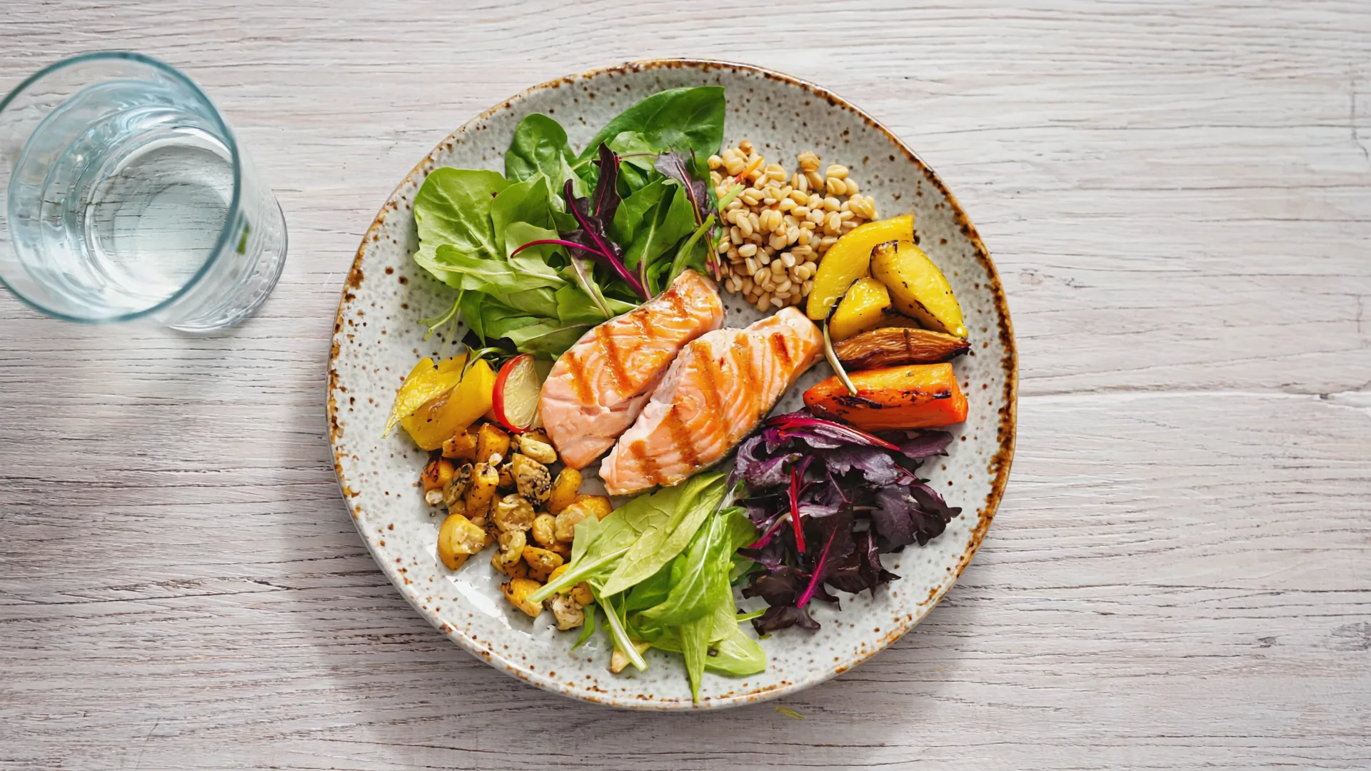 An overhead view of a balanced, colourful healthy meal with salmon, vegetables and wholegrains on a wooden table