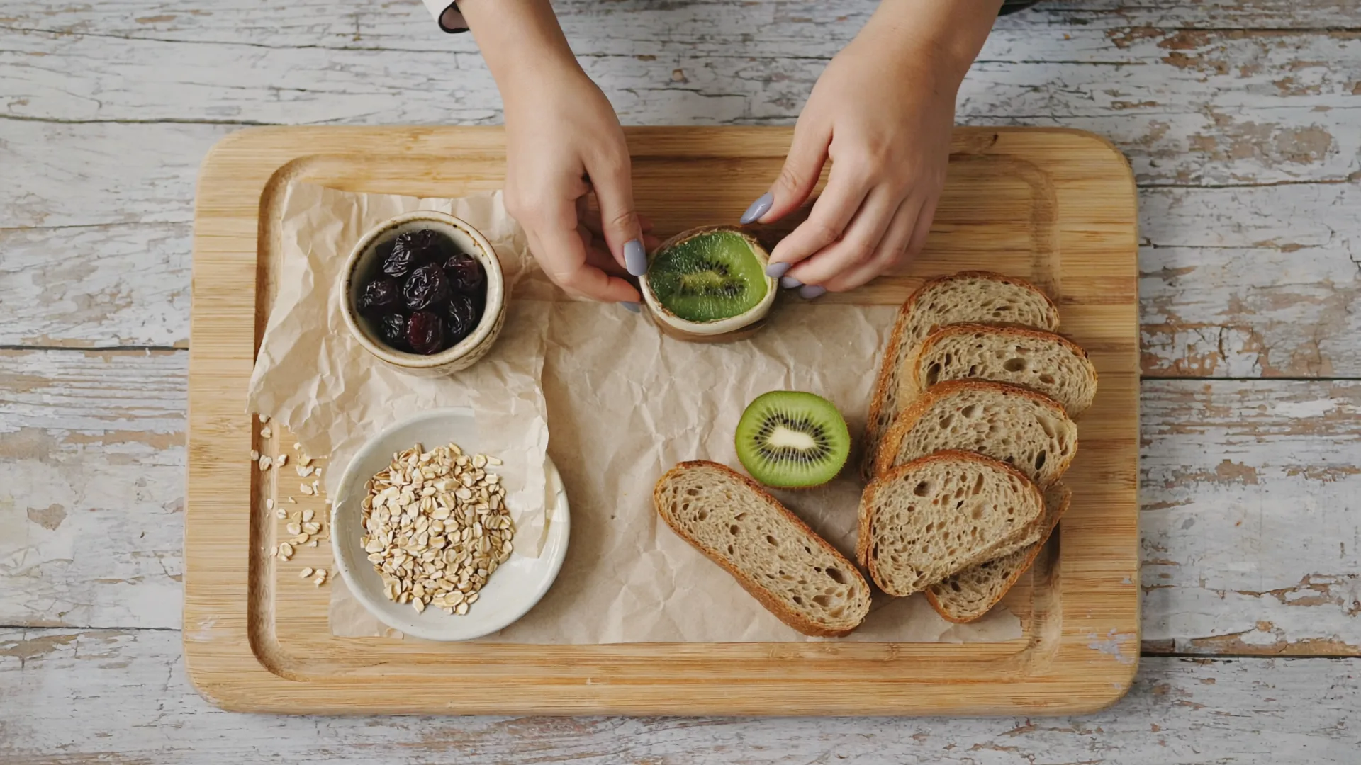 Rolled oats, linseed, dried prunes, halved kiwi fruit and wholemeal bread arranged on a rustic wooden board